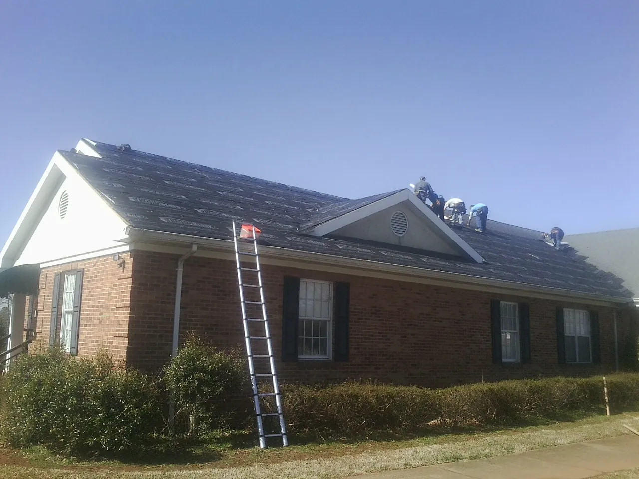 Crew tearing shingles off a brick ranch roof with a ladder set — Metal Roof Repair work by our crew in Olney