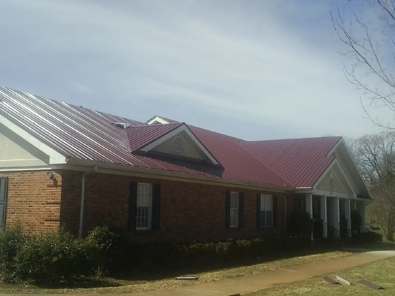 Red metal roof with gabled entries on a long brick building, from a Hail Damage Roof Repair job in Olney