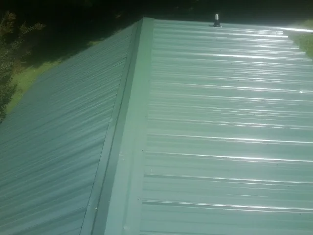 New green metal panels meeting at the ridge of a roof — Flat Roof Repair work by our crew in Olney